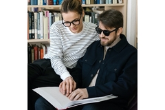 A woman helping a blind man read.